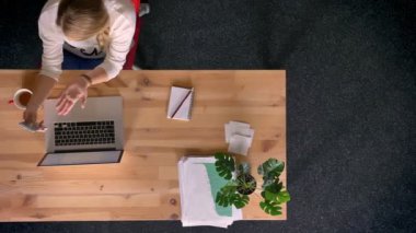 Dolly atış yukarıdan aşağıya görünümünü raslantı giyimli kadın ofiste laptop önünde smartphone kullanarak görüntülü sohbet söz.