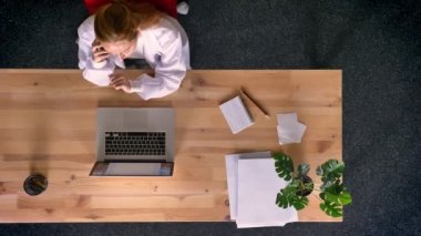 Dolly vurdu, telefonda konuşmak ve belgili tanımlık laptop önünde gesticulating laboratuar önlüğünü yukarıdan aşağıya zencefil kadın görünümünü giymiş