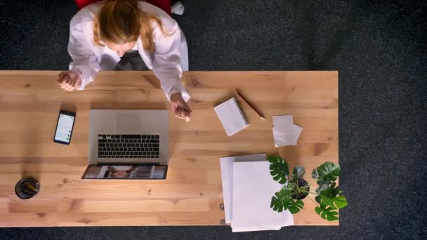 Снимок Долли, вид сверху на рыжую женщину в халате, разговаривающую в видеочате с помощью ноутбука в офисе . — стоковое видео
