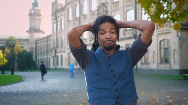 Portré, fiatal afro-amerikai srác a dreadlocks üzembe a kezét a háta mögött, a szórakoztató egyetemi háttér. — Stock videók