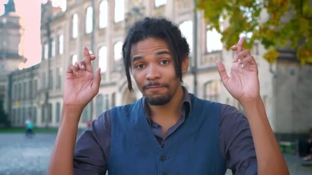 Närbild porträtt av afro-amerikansk student med dreadlocks korsar fingrarna och hoppas på lycka på universitet bakgrund. — Stockvideo