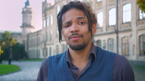 Portrait d'un étudiant afro-américain attrayant avec dreadlocks agitant négativement la tête sur fond universitaire . — Video