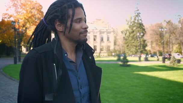 Rundumblick auf afrikanisch-amerikanische Studentin mit Dreadlocks, die durch herbstlichen Park geht und jemanden begrüßt. — Stockvideo