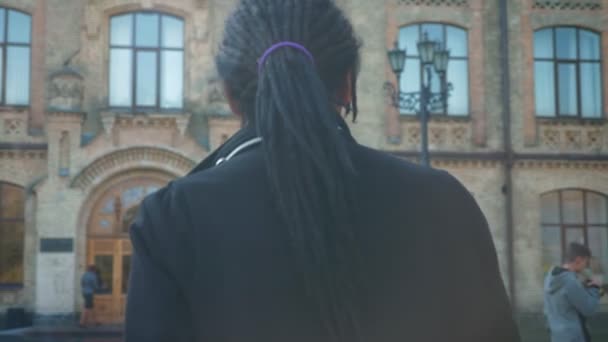 Close-up rear-view of young African-American student with dreadlocks going to university in sunshine. — Stock Video