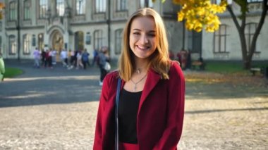 Genç kız öğrenci, üniversite arka plan üzerinde bir kamera ayakta bakıp gülüyor