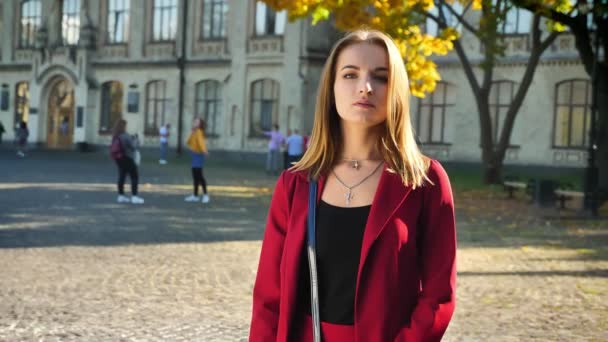 Young female student looking on a camera standing on the background of university in a serious mood — Stock Video