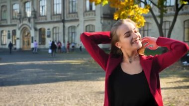 Genç kız öğrenci mutlu saç sallayarak ve gülüyor, bir kameraya bakarak, Üniversitesi, açık havada arka plan üzerinde duran