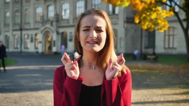 Young female student is worried and nervous, with her fingers crossed before an exam, outside the university — Stock Video