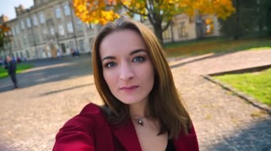 Telefonunu kameraya bakarak, saçları ile oyun ve üniversitenin dışında gülümseyen çekici genç kız öğrenci