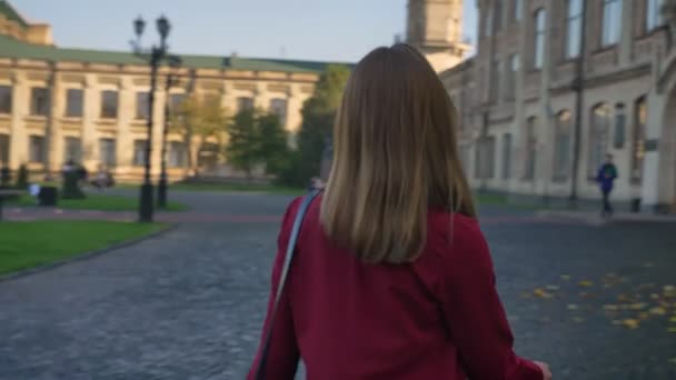 Молодая привлекательная женщина, студентка, идущая в университет, уверенно и мотивированная на фоне других студентов — стоковое видео
