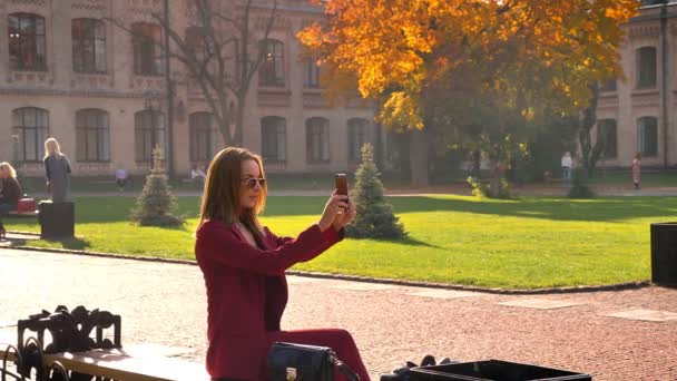 Young attractive female student sitting in the university square and taking selfie in a sunny warm day — Stock Video