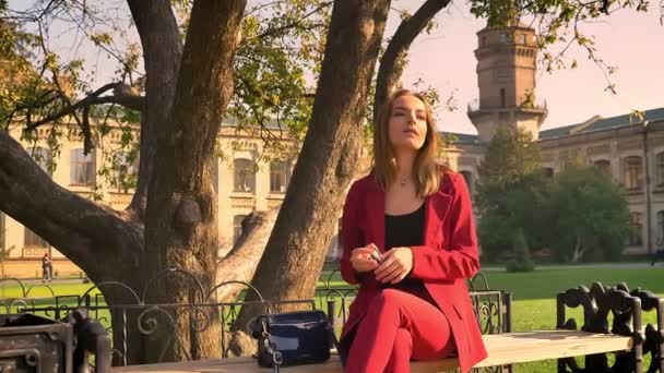 Young attractive female student sitting in the university square taking off sunglasses and being amused by beautiful sunny day — Stock Video