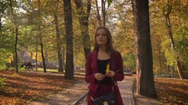 Düşünceli attrractive kadın parkta elinde sarı yaprak ile yürüme ve güneşli bir sonbahar günü içinde etrafa.