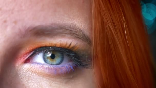 Detail napůl portrét zázvor ženské barevné oční make-up na pozadí rozmazané modrých světel. — Stock video