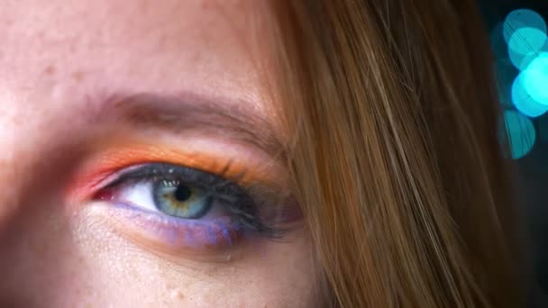 Nahaufnahme-Halbporträt einer blonden Frau, die in die Kamera schaut, mit buntem Augen-Make-up auf blauem Lichterhintergrund. — Stockvideo