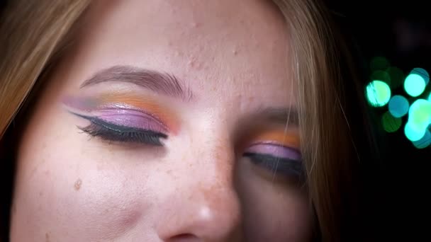 Close-up portret van blonde vrouwen kijken naar boven en naar camera met kleurrijke oog make-up op groene lichten achtergrond. — Stockvideo