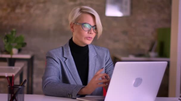 Retrato de mujer de negocios de pelo corto de mediana edad en gafas hablando en videochat usando computadora portátil en la oficina . — Vídeos de Stock