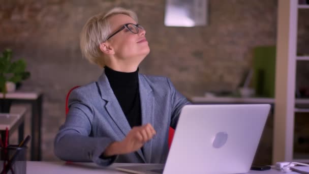 Портрет короткошерстої бізнес-леді в окулярах, що танцює на своєму сидінні в офісі . — стокове відео