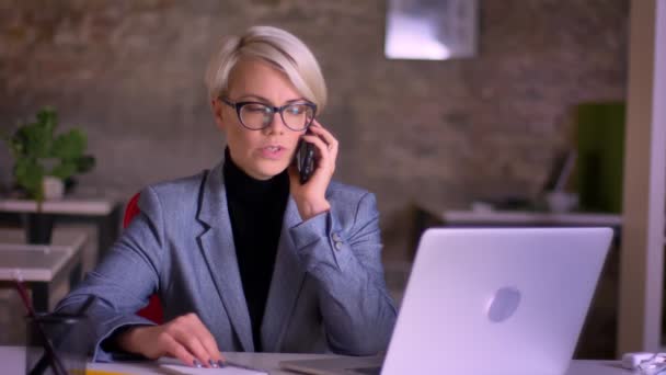 Портрет блондинки короткошерстої бізнес-леді в окулярах серйозно розмовляє на мобільному телефоні в офісі . — стокове відео