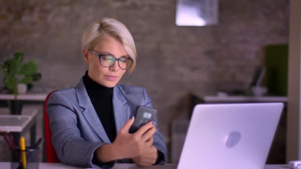 Retrato de meia-idade loira mulher de negócios de cabelos curtos em óculos fazendo selfie-foto usando celular no escritório . — Vídeo de Stock