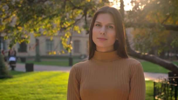 Retrato de una joven morena mirando a la cámara con sonrisa sobre fondo verde del parque . — Vídeos de Stock