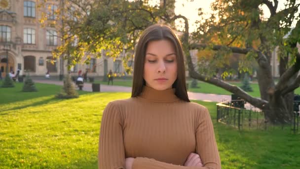 Jeune fille brune caucasienne regarde dans la caméra avec fierté et rage sur fond de parc vert . — Video