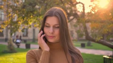 Yeşil park arka plan telefonda konuşurken çekici esmer gerl portresi.