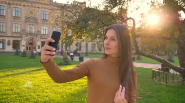 Güzel esmer yeşil park arka plan üzerinde onun smartphone kullanarak selfie fotoğraf yapma portresi.