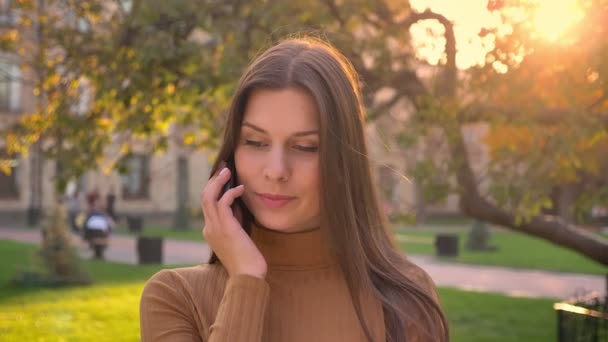 Porträtt av attraktiv brunett gerl talar på mobiltelefon på grön park bakgrund. — Stockvideo