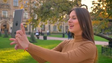 Görüntülü sohbet konuşmak ve onun tablet kullanarak yeşil park arka plan gösteren güzel esmer kız portresi.