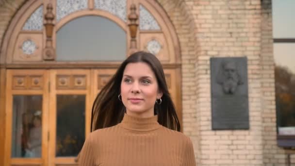 Portré, fiatal, mosolygós kaukázusi lány séta a hop az épület mentén őszi park — Stock videók