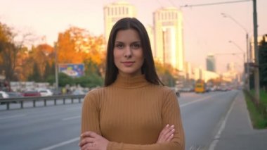 Portre Genç beyaz esmer içine kamera mütevazı gülümseme ve kolları ile seçkin örneklerini izlemenin yol arka plan üzerinde çarpı işareti.