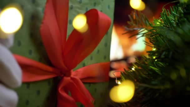 La mano de Papá Noel pone un regalo sobre la mesa. Navidad tres en brillo chimenea bokeh luces fondo — Vídeo de stock