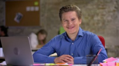 Gülümseyen ve kamera Office göz kırpıyor laptop önünde orta yaşlı sarışın işadamı portresi.