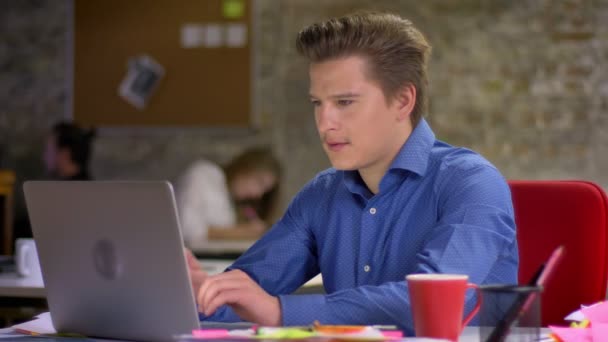Portret van middelbare leeftijd blond zakenman die op laptop in kantoor te typen op een stoel versteld en drinkt koffie met tevredenheid. — Stockvideo