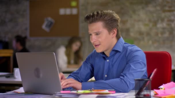 Retrato de hombre de negocios rubio de mediana edad feliz delante de la computadora portátil lograr el éxito y poner las manos hacia arriba en la oficina . — Vídeo de stock