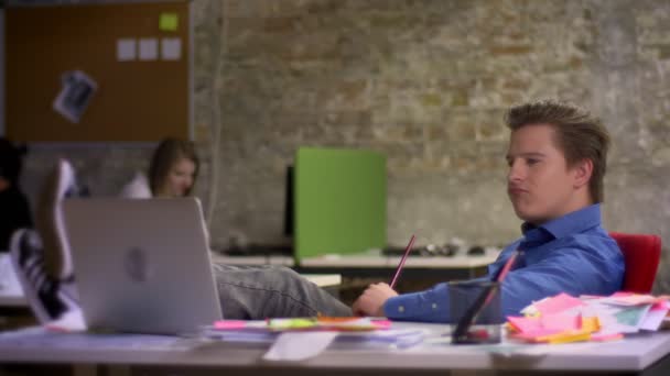 Homme d'affaires blond d'âge moyen avec les jambes sur le bureau est surpris et montre de manière satisfaisante dans un ordinateur portable au bureau . — Video