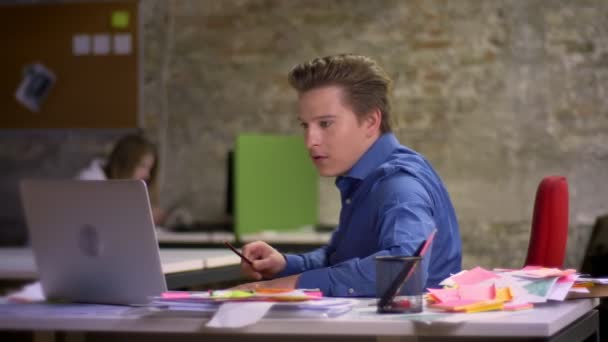 Empresário loiro de meia-idade com pernas na mesa fica divertido e satisfatoriamente assiste no laptop e, em seguida, na câmera no escritório . — Vídeo de Stock