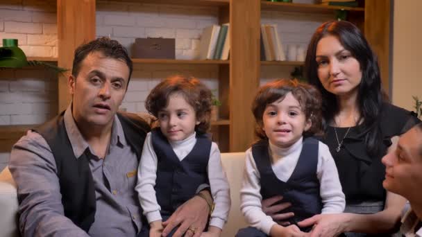 Familia árabe sentada en el sofá y mirando positivamente en la cámara en la sala de estar . — Vídeos de Stock