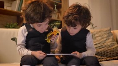 Kanepede oturan ve interestedly tablet oturma odasında içine izlerken küçük Arapça kıvırcık kafalı ikizler portresi.