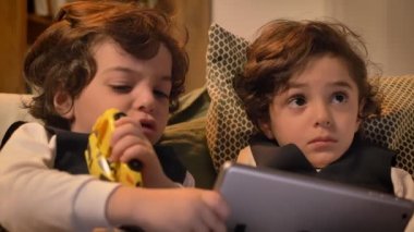 Kanepede oturan ve interestedly tablet oturma odasında içine izlerken küçük Arapça kıvırcık kafalı ikizlerin yakın çekim portre.
