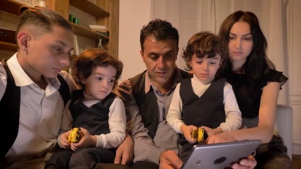 Portrait of arabic family sitting on sofa and watching attentively into tablet in living room in cosy atmosphere. — Stock Video