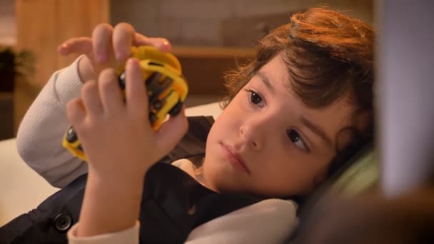 Close-up portret van schattige Arabische krullend hoofdige jongen liying op de Bank en te spelen met speelgoed in de woonkamer. — Stockvideo