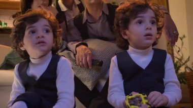 İki Arap kıvırcık kafalı ikiz dikkatle onların aile arka plan üzerinde Tv izlerken oturma odasında katta oturan portresi.