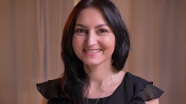 Yakın çekim portre Arapça esmer anne doğrudan içine soluk arka plan üzerinde hoş gülümseme ile kamera izliyor.