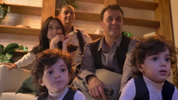 Portrait of two cute arabic curly-headed twins sitting on floor in living room carefully watching TV with their family on background. — Stock Video