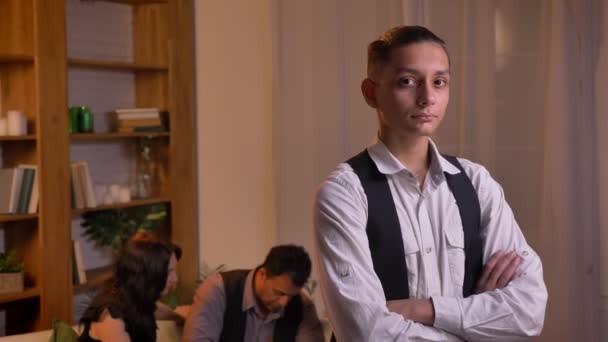 Retrato de un adolescente árabe mirando directamente a la cámara con los brazos cruzados y a su familia de fondo . — Vídeos de Stock