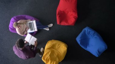 Üst-shot dizüstü bilgisayar ile genç kadın ve adam birbirleri ile rengarenk çanta arka plan üzerinde konuşurken defter ile.