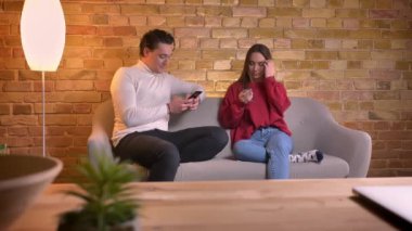 Akıllı telefonlar ile kanepede oturan ve birbirleri ile ev atmosferde konuşan genç çift portresi.