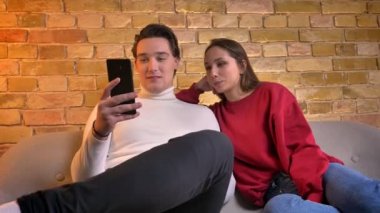 Smartphone dikkatle izliyor ve mutlu bir şekilde birbirleri ile ev atmosferde konuşurken beyaz arkadaş portresi.